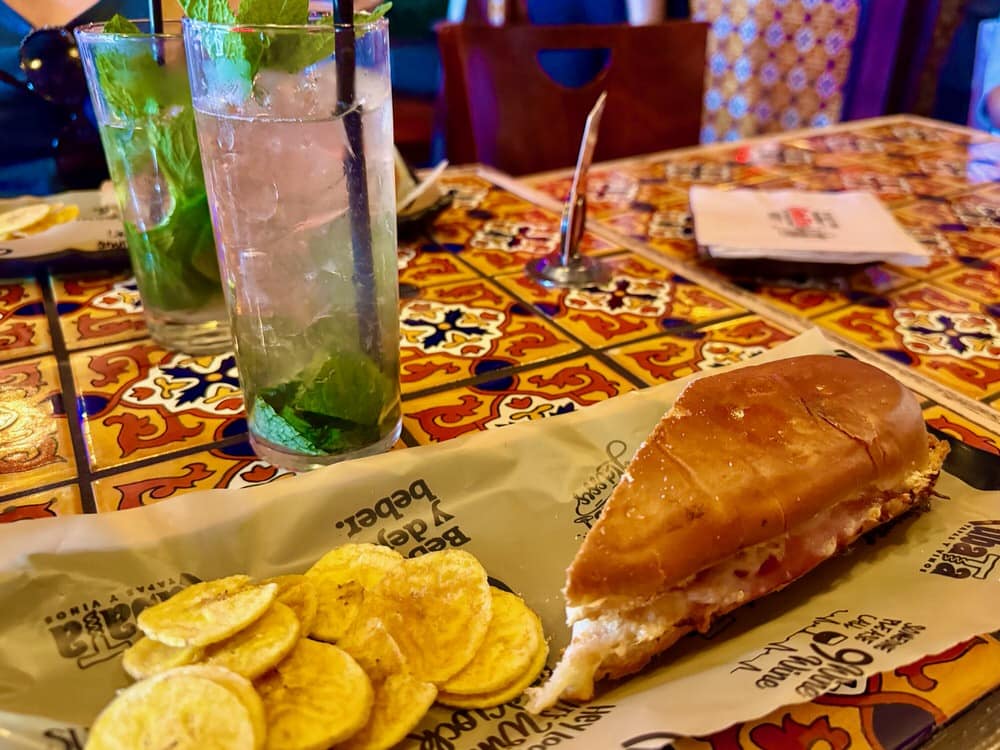 Half a cubano sandwich sits on a paper covered platter with a side of plantain chips in a restaurant in Miami's Little Havana.